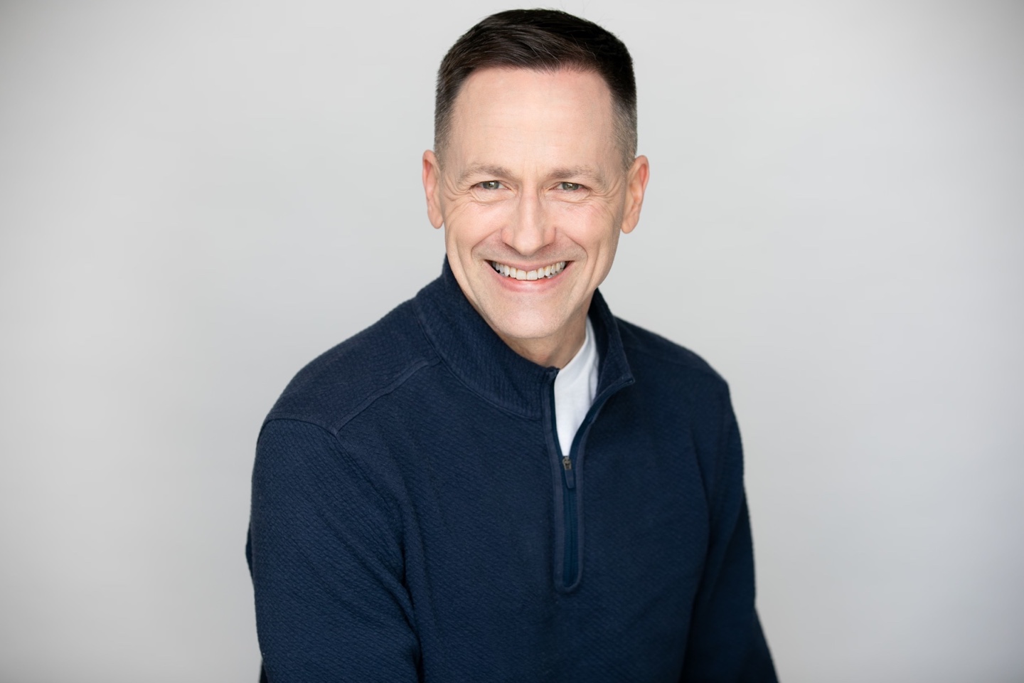 Fletcher Shepley smiling warmly in a navy sweater against a pale gray background