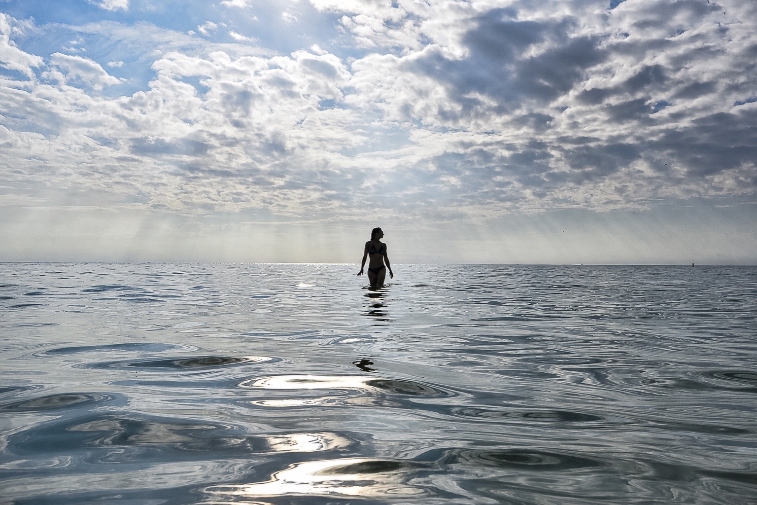 Ariel standing in calm ocean water beneath a luminous, cloud-filled sky