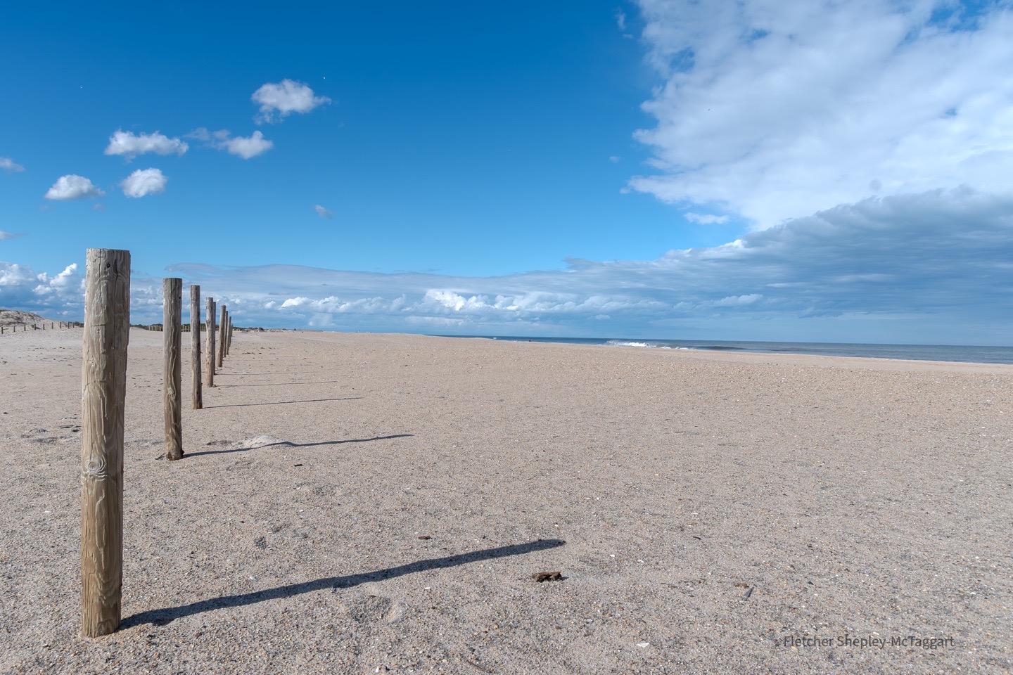 A minimal beach with weathered posts sits beneath a broad blue sky.